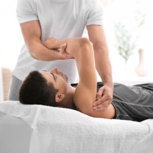 ein Mann liegt auf einem Bett und streckt seinen Arm aus. Es geht um Microkinesitherapie